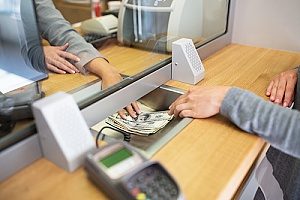 a bank teller handing withdrawn money to an individual with a personal checking account